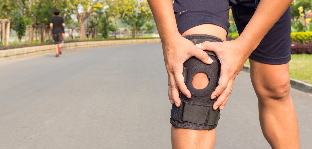 runner gripping his knee in a knee brace